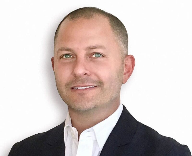 Smiling man in a suit with a white shirt against a plain white background.