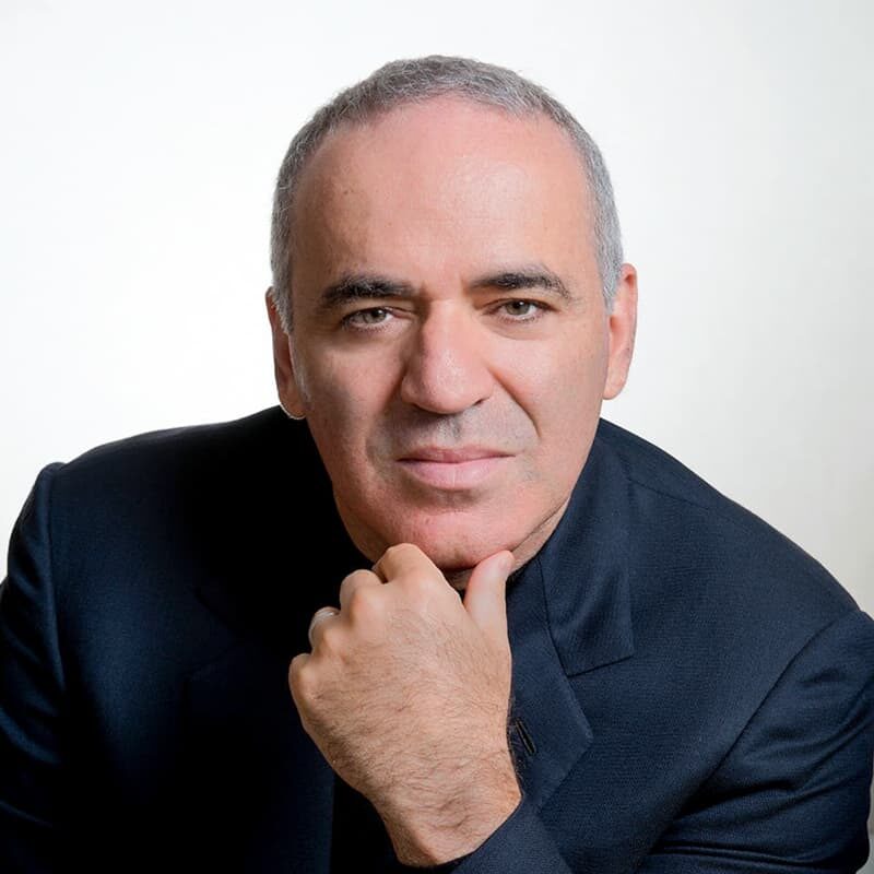 A person with short, gray hair wearing a dark suit jacket, resting their chin on their hand, and looking directly at the camera against a light background.