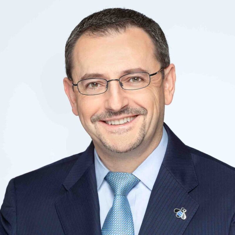 Smiling man in a suit with glasses and a tie against a plain background.