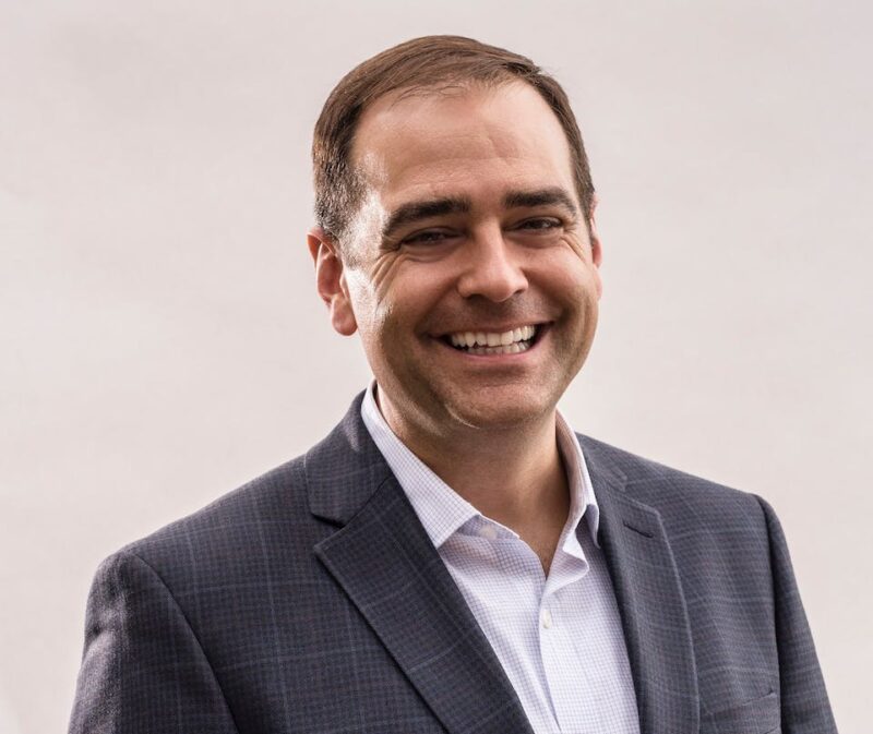 Smiling man in a suit against a plain background.