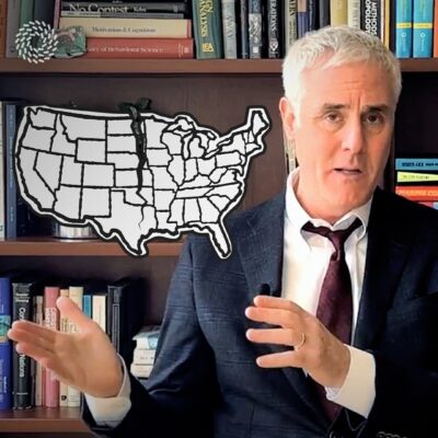 Man in a suit gestures with hands in front of bookshelves, with a map outline of the USA in the background.