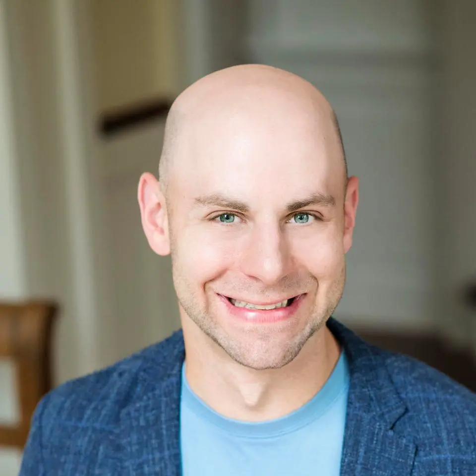 Smiling bald man wearing a blue shirt and blazer, indoors.