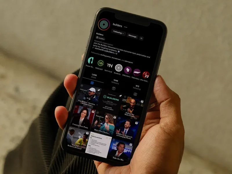 Hand holding a smartphone showing a social media profile with videos and posts in dark mode.